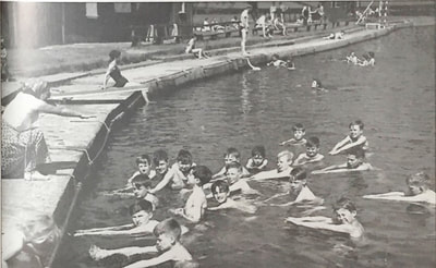 Pupils of Penrith Boys' National School kept cool in an open-air 'classroom' when they visited the bathing place of Penrith Swimming Club, in the River Eamont at Frenchfield. The instructress, Mrs. Cuthbert, demonstrated strokes from the bank.

Credit: Time of Change - Eric Davidson